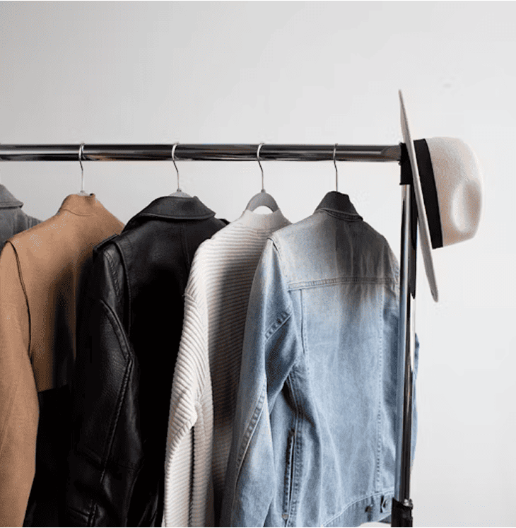 various clothes hanging on a clothes rack in front of a light brick wall