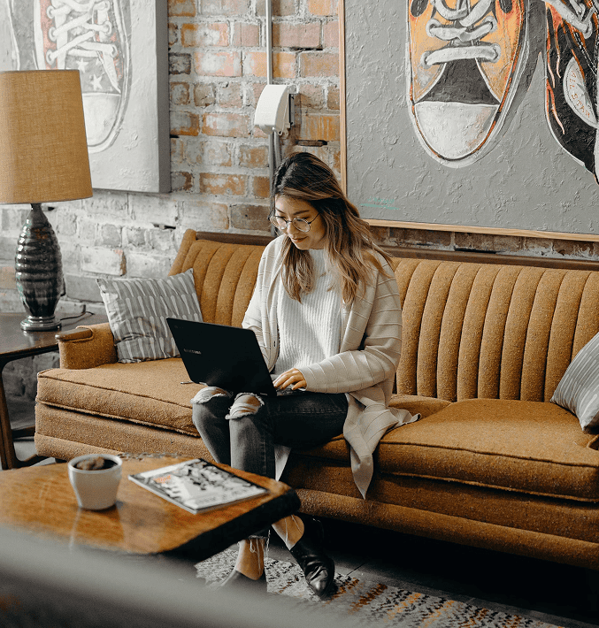 young woman in an urban designed apartment sitting on a couch with a laptop