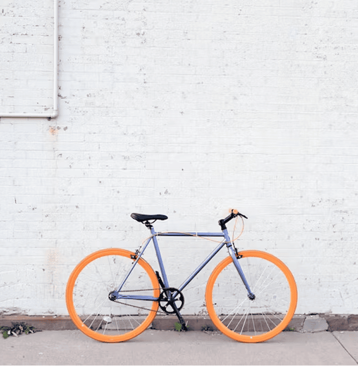 a blue bike with orange wheels leaning against a light brick wall